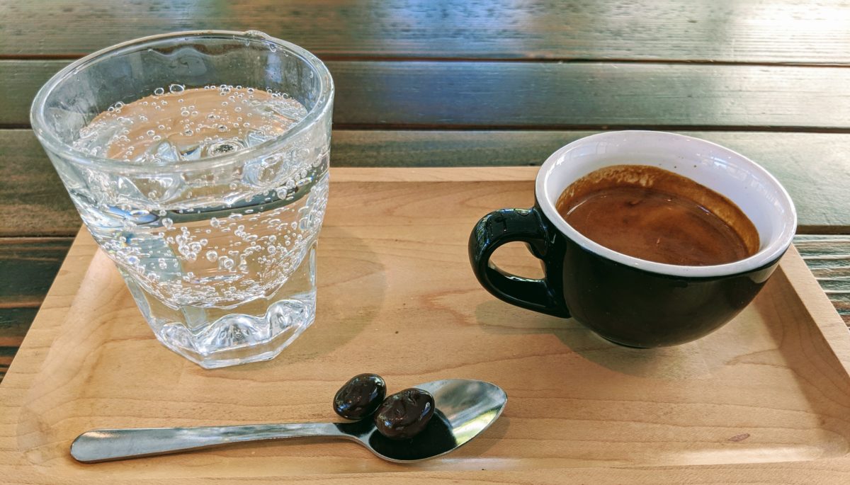 A tray with sparkling water, espresso, and chocolate covered espresso beans.